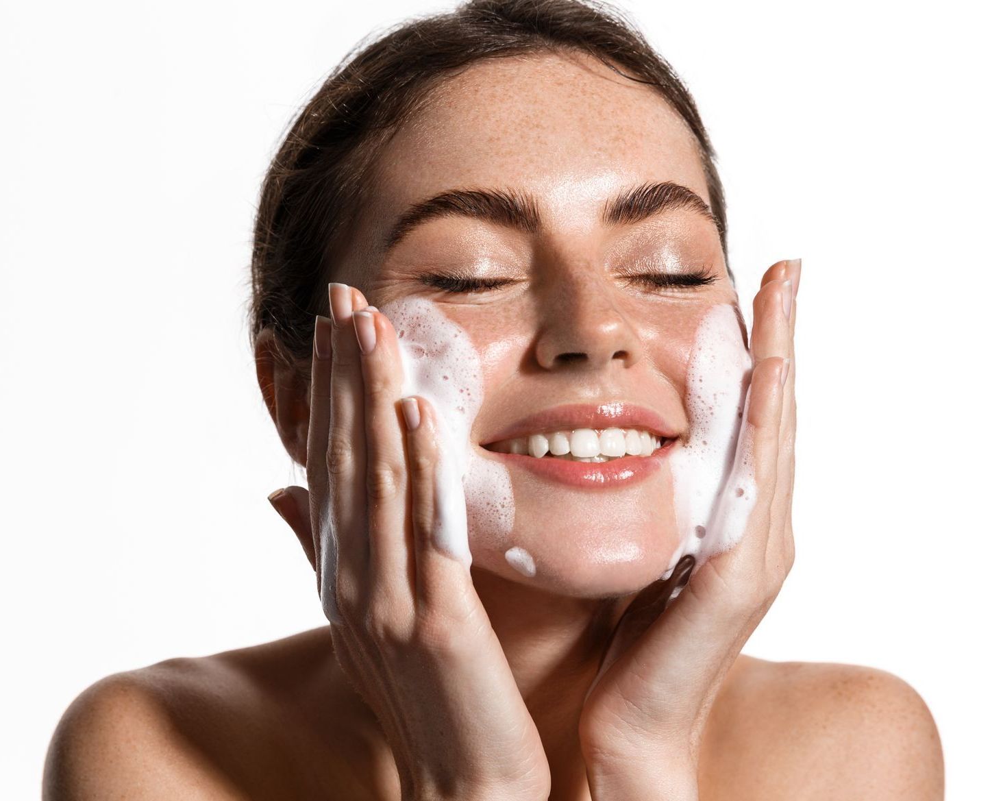 A woman is smiling while washing her face with soap.
