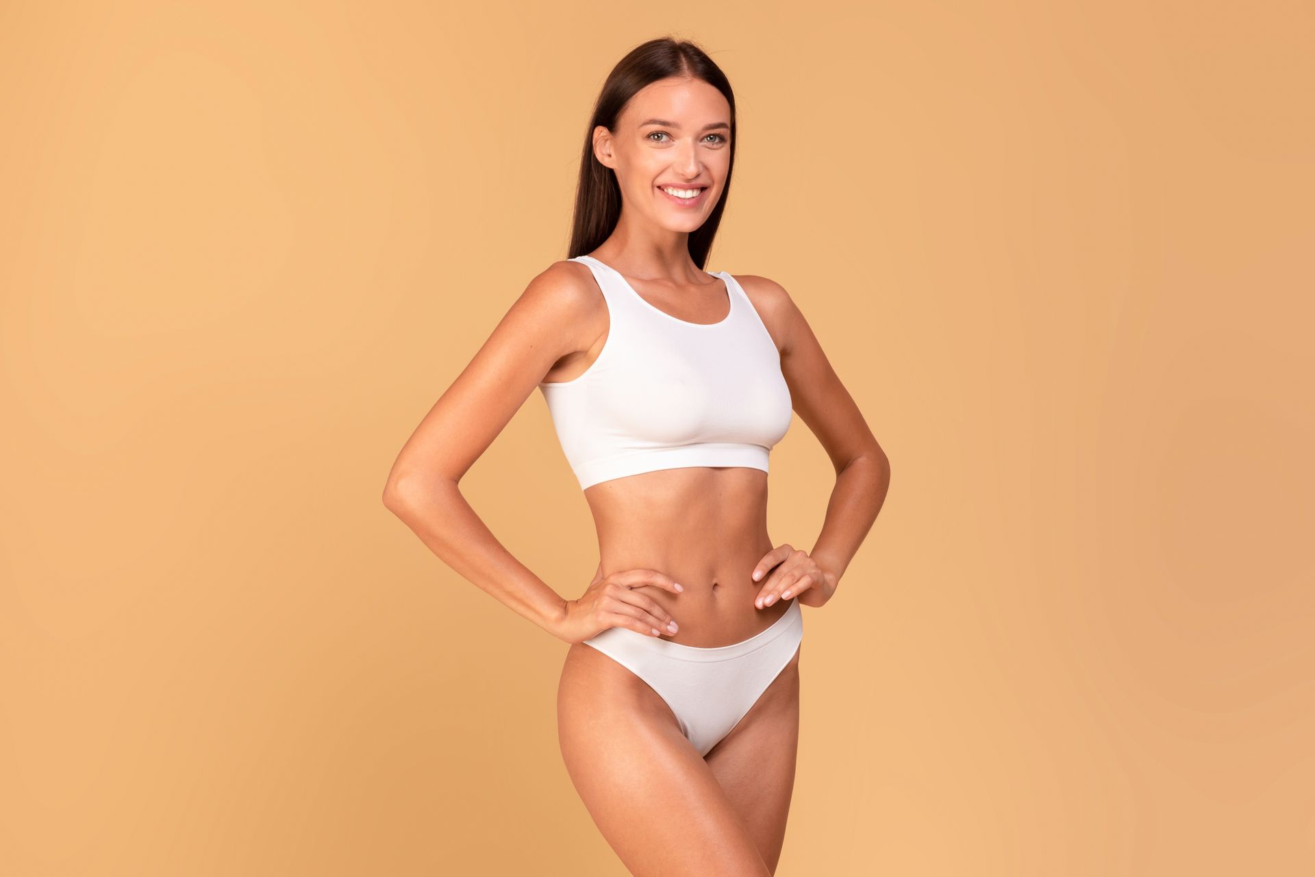 A woman in white underwear is standing with her hands on her hips and smiling.
