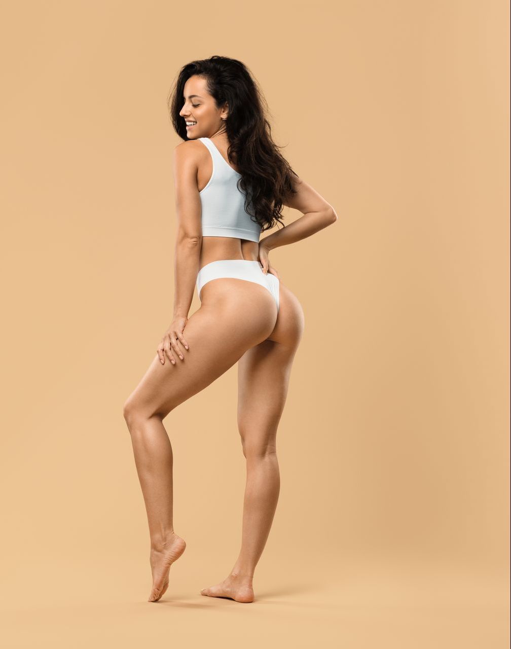 A woman in white underwear is standing on a beige background.