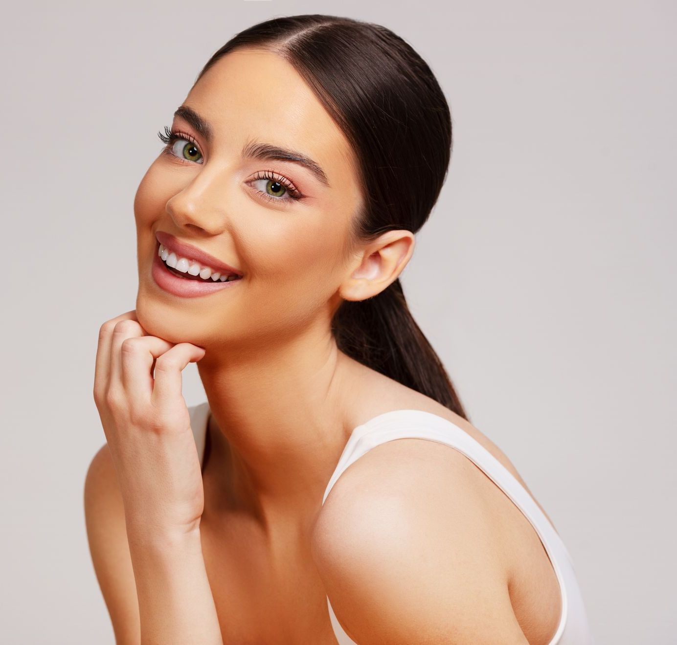A woman is smiling and touching her face with her hand.