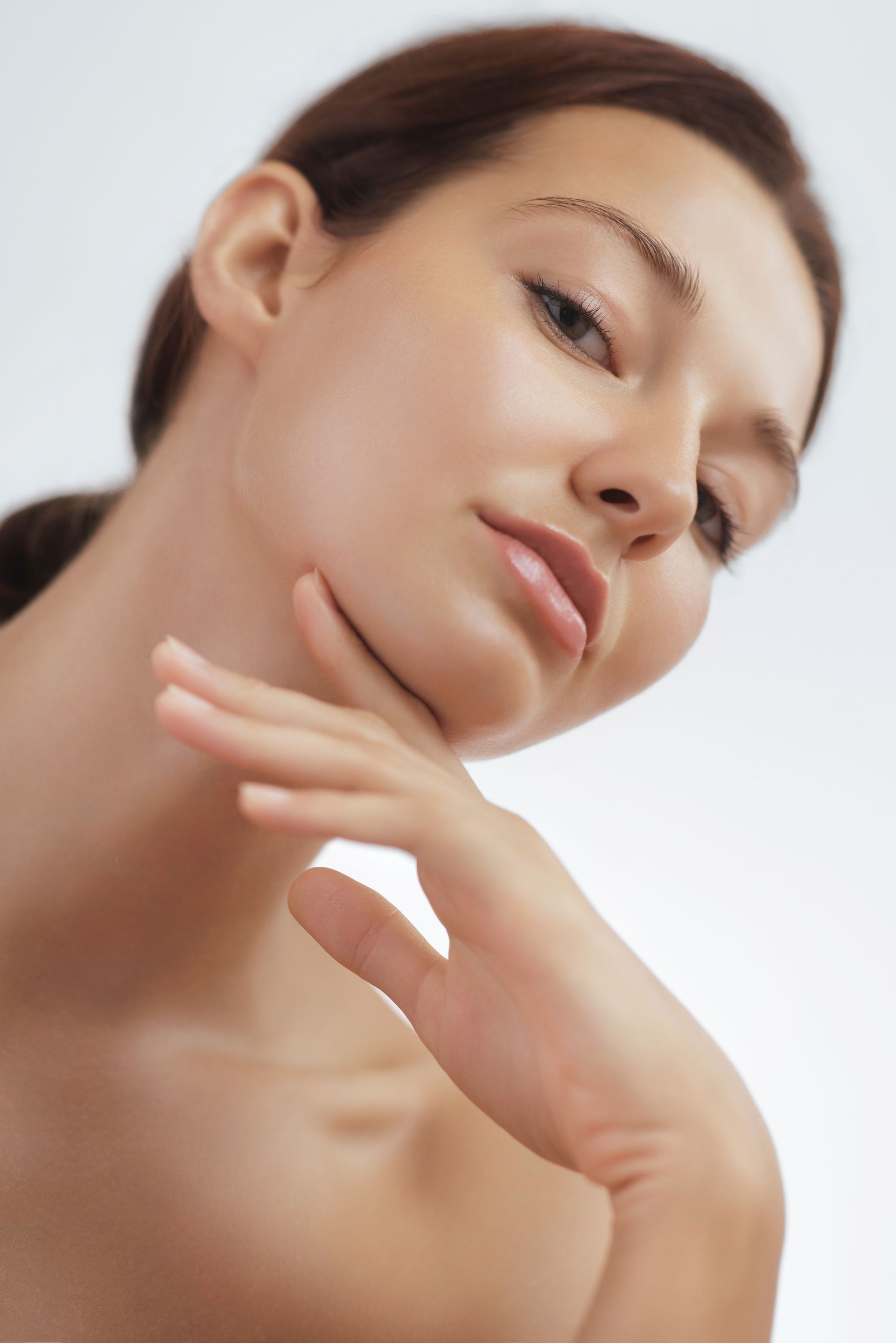 A woman is touching her neck with her hand and looking at the camera.