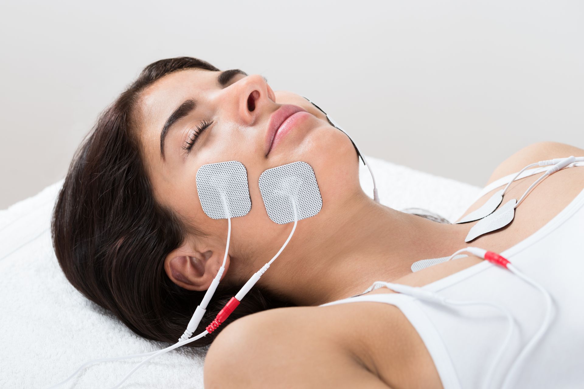 A woman is laying on a bed with two electrodes on her face.