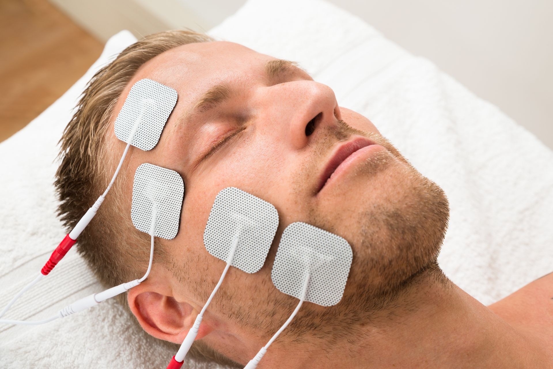 A man is laying on a bed with electrodes on his face.