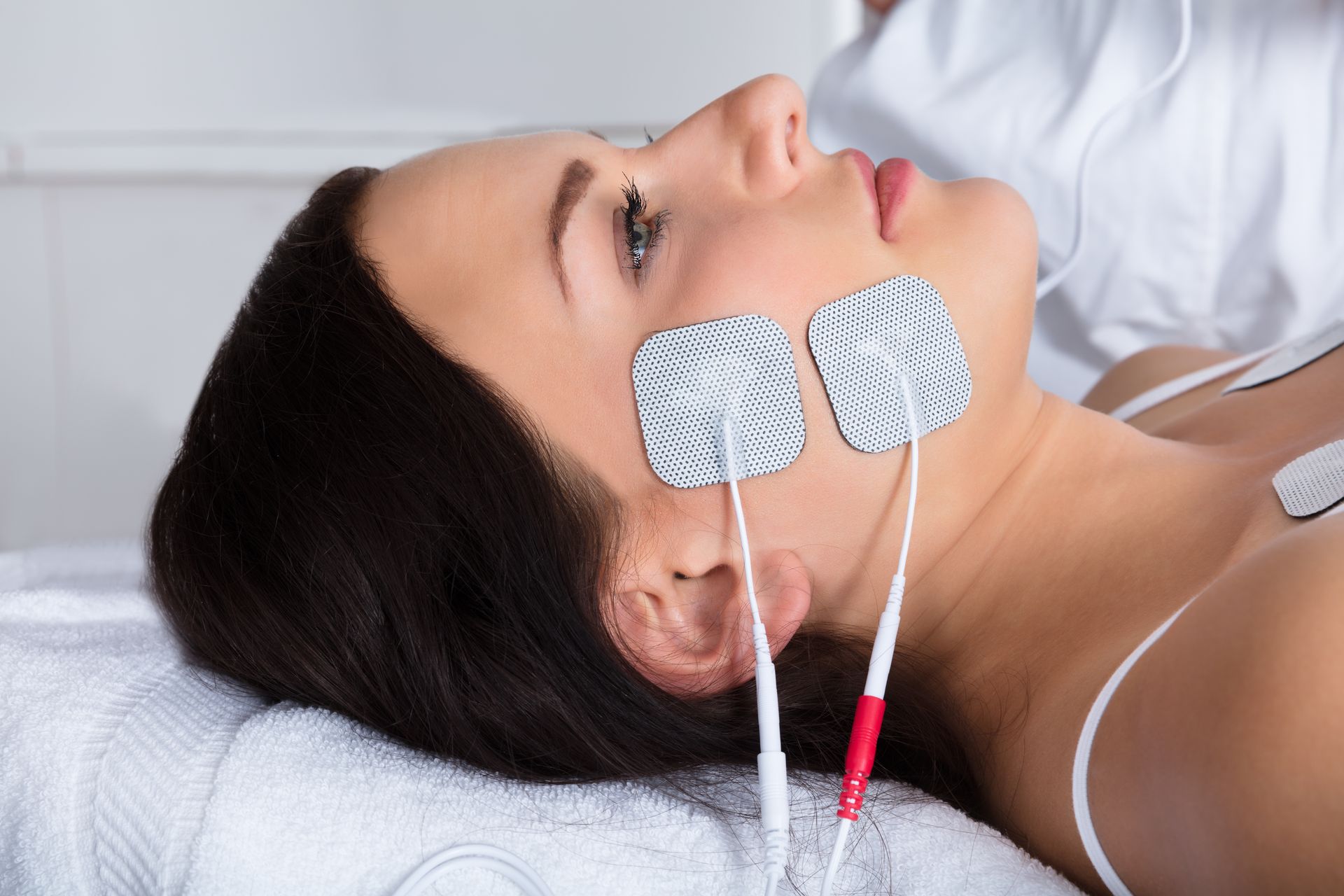 Woman receiving facial electrotherapy treatment with electrode pads.