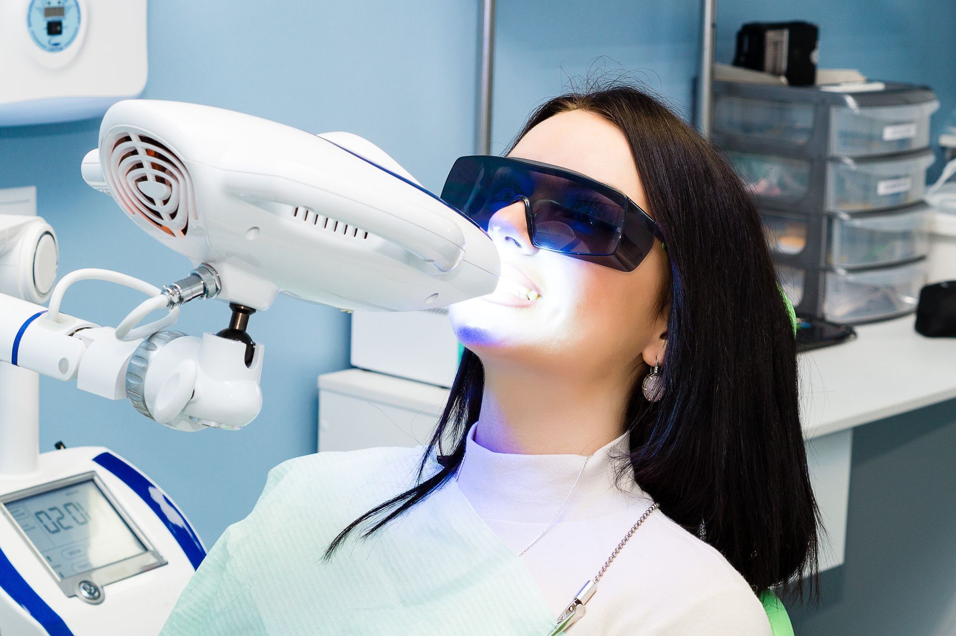 A woman is getting her teeth whitened in a dental office.