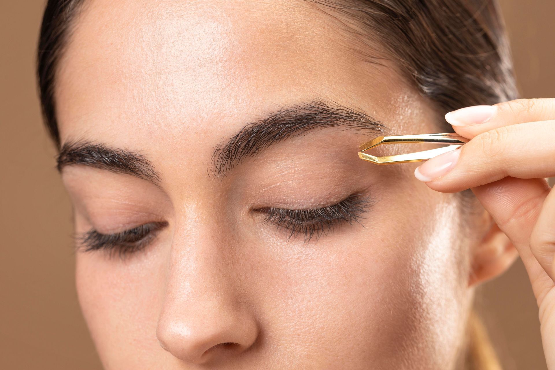 A woman is using tweezers to trim her eyebrows.