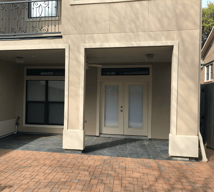 alight brown house with pale brown stucco walls, there are French doors at the bottom of the house and a black balcony on the first floor