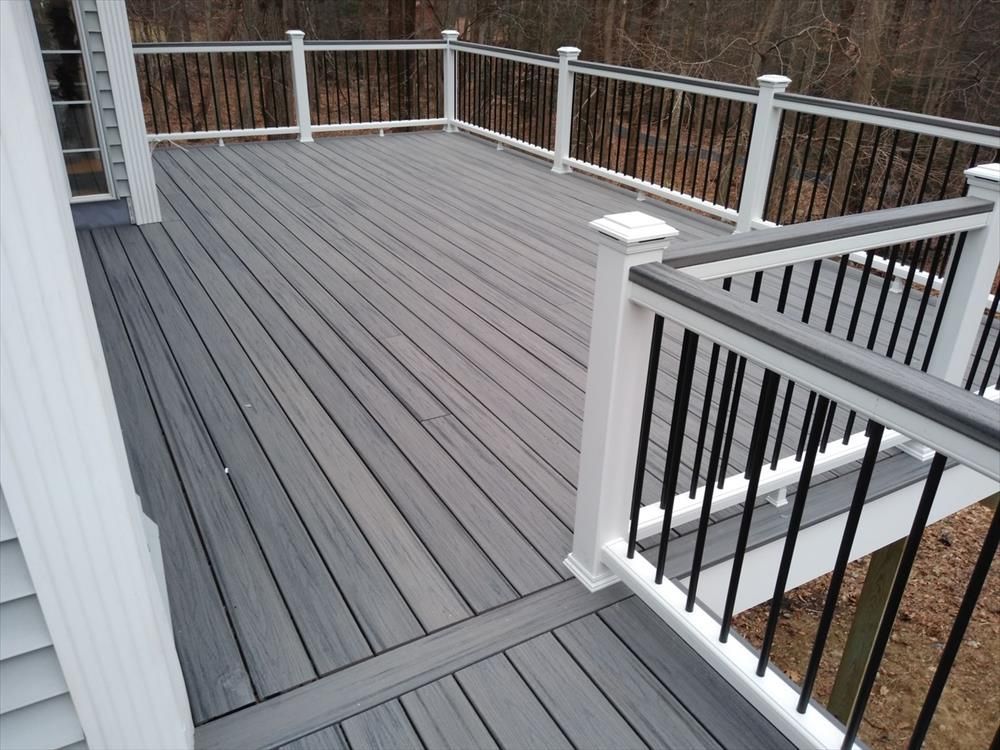 Gray composite deck with white and black railings, surrounded by trees.