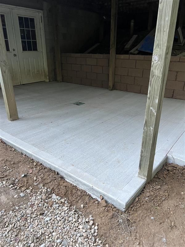 A concrete patio with wooden posts and a brick wall in the background.