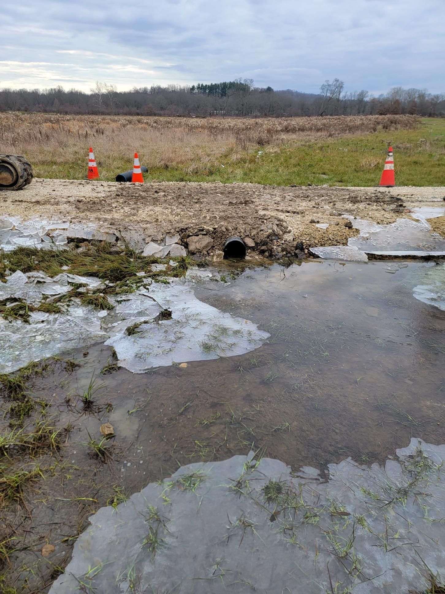 A pile of pipes and concrete rings are stacked on top of each other on a dirt field.