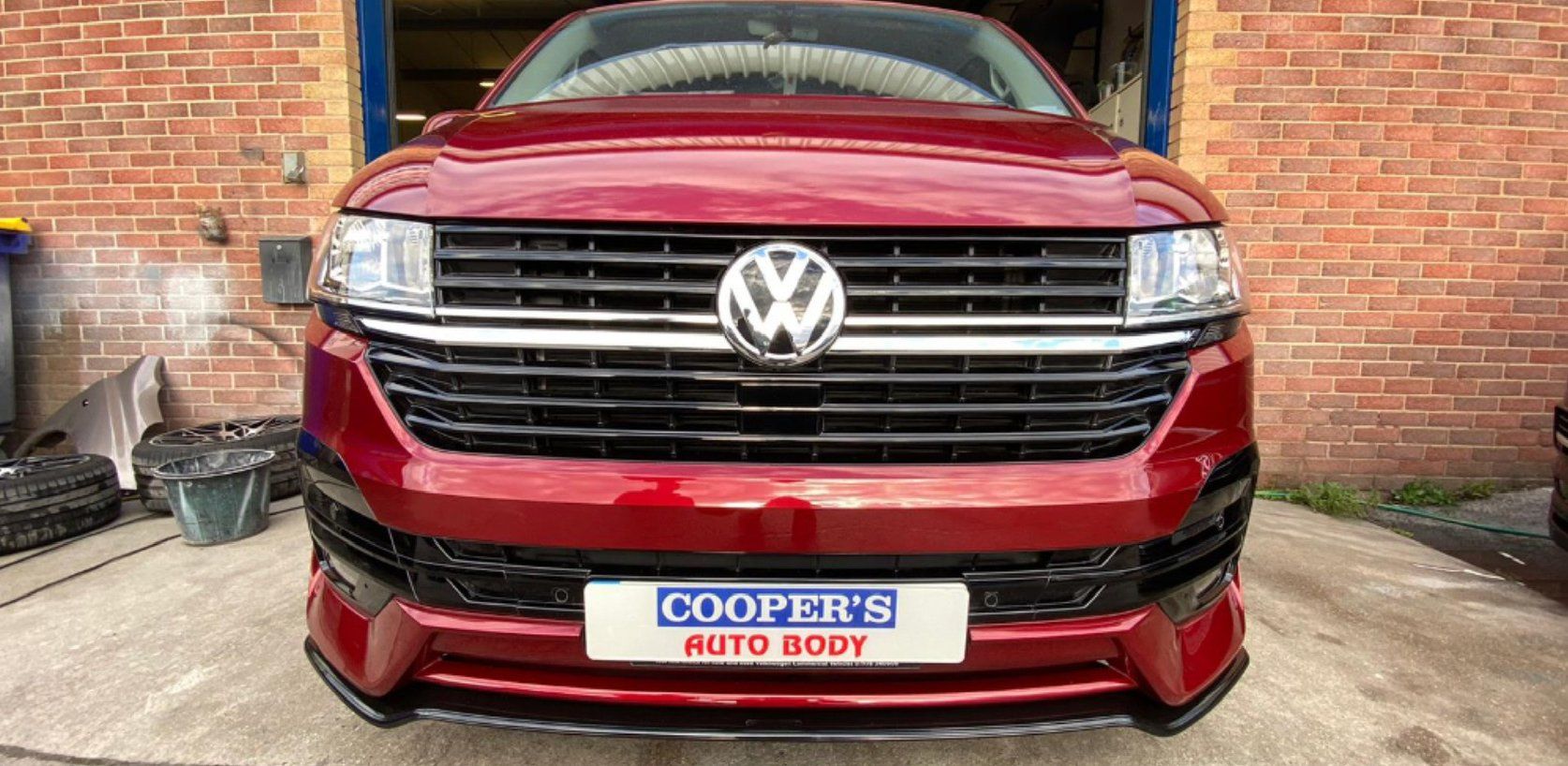 Red Volkswagen van at Cooper's Auto Body shop, with a black grill, and badge.