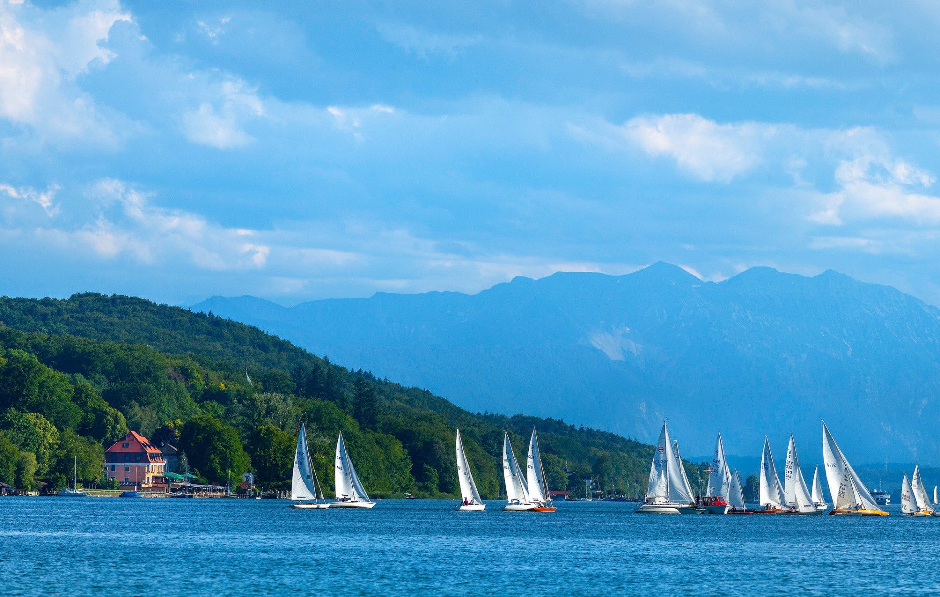 Mehrere Segelboote auf ruhigem See mit Bergen im Hintergrund, ideal für Aktivurlaub in Bayern.