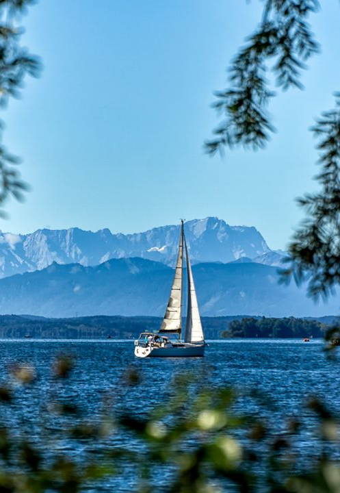 Segelboot mit weißem Segel auf glitzerndem Wasser zwischen zwei dunklen Pfosten unter klarem, blauem Himmel
