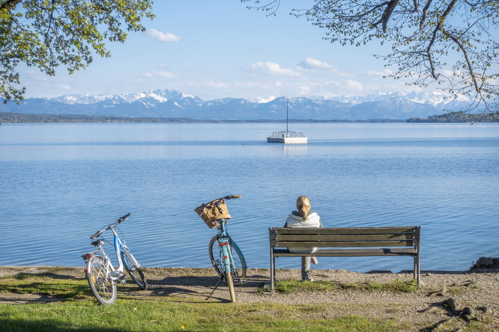 Person sitzt auf Bank am bayerischen See mit Blick auf Alpen.