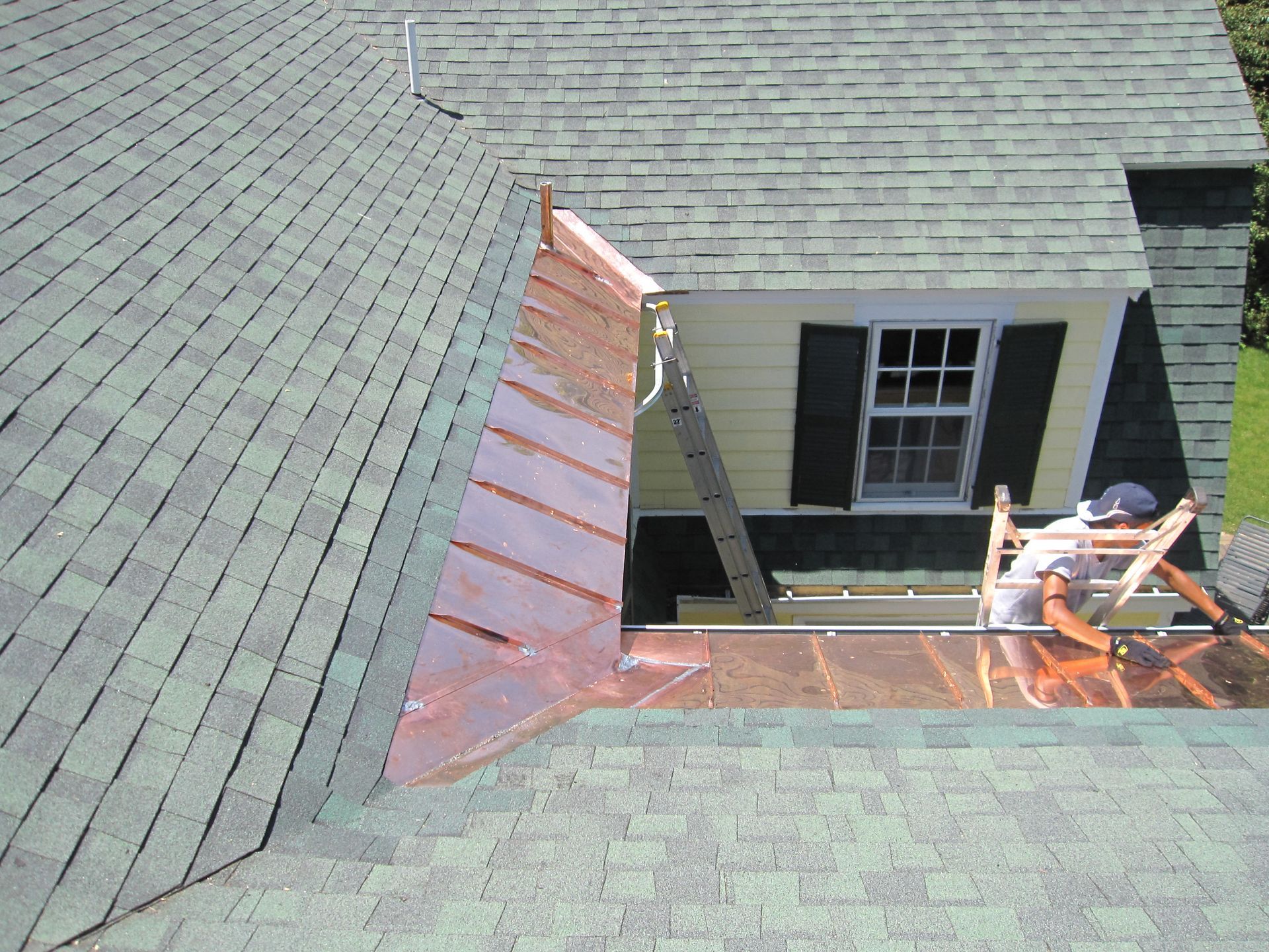 A man on a ladder is working on a copper roof