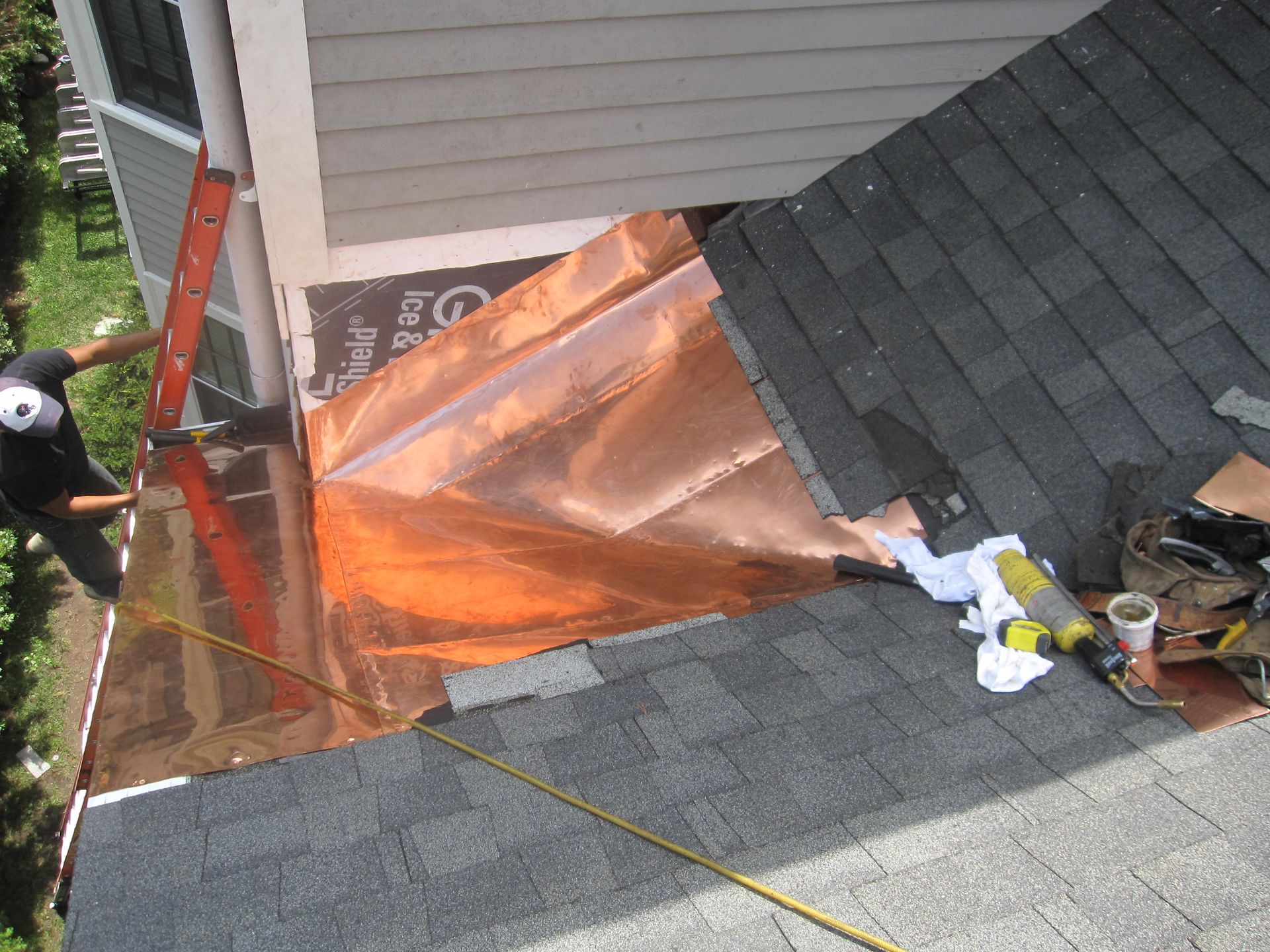 A man on a ladder is working on a copper roof