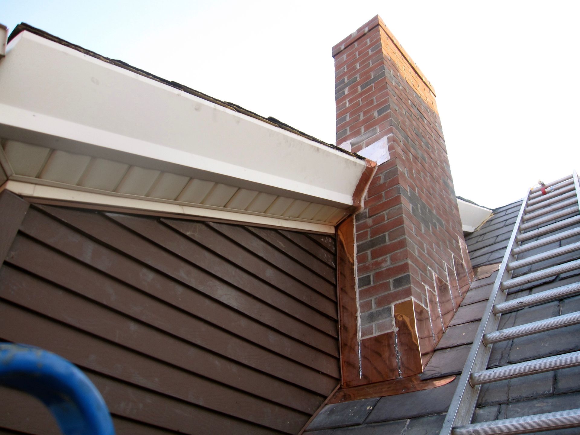 A ladder is sitting on top of a roof next to a chimney