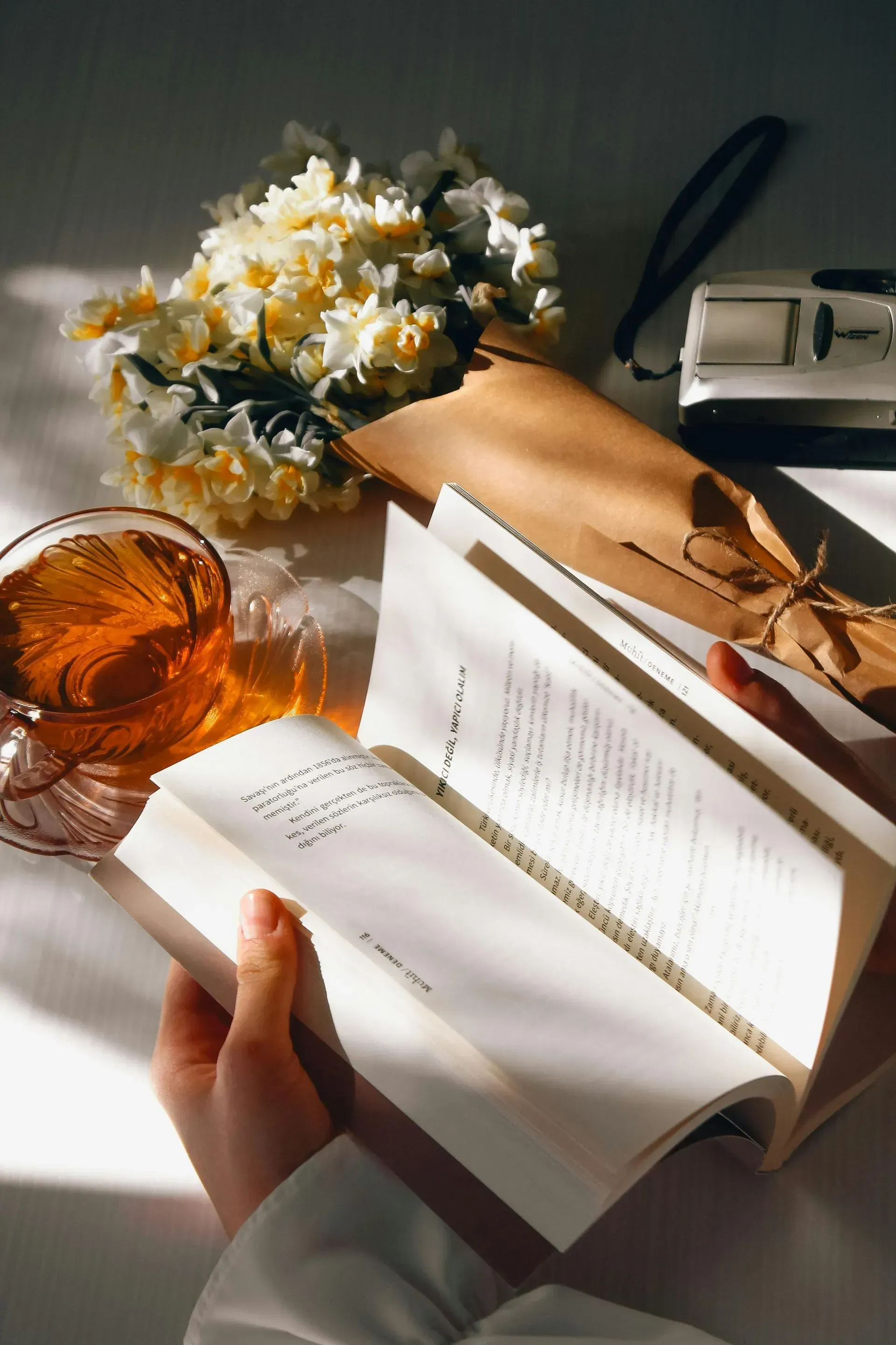 reading a book, with tea and flowers on the desk