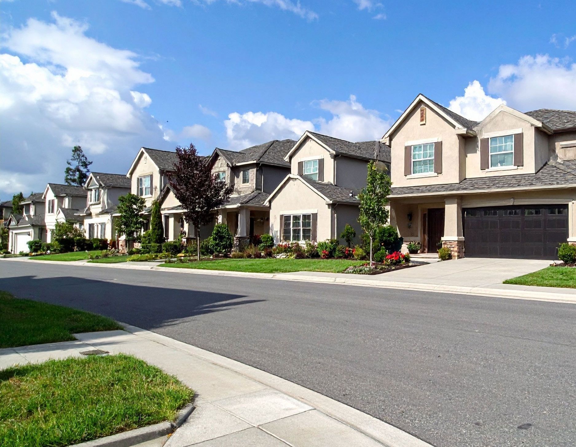 Row of houses on a sunny street with blue sky and white clouds. Row of beige houses along a suburban street under a blue sky with fluffy clouds in Charlotte, NC