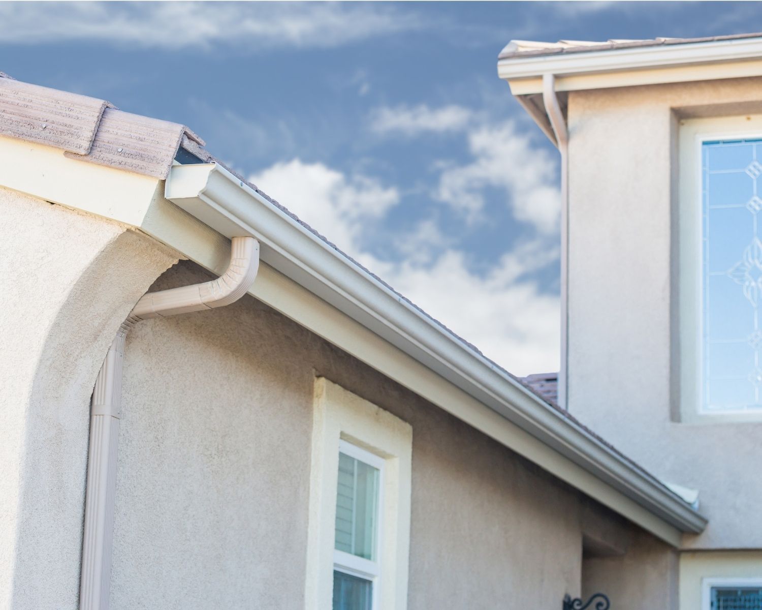 Beige house exterior with gutters under a blue sky.