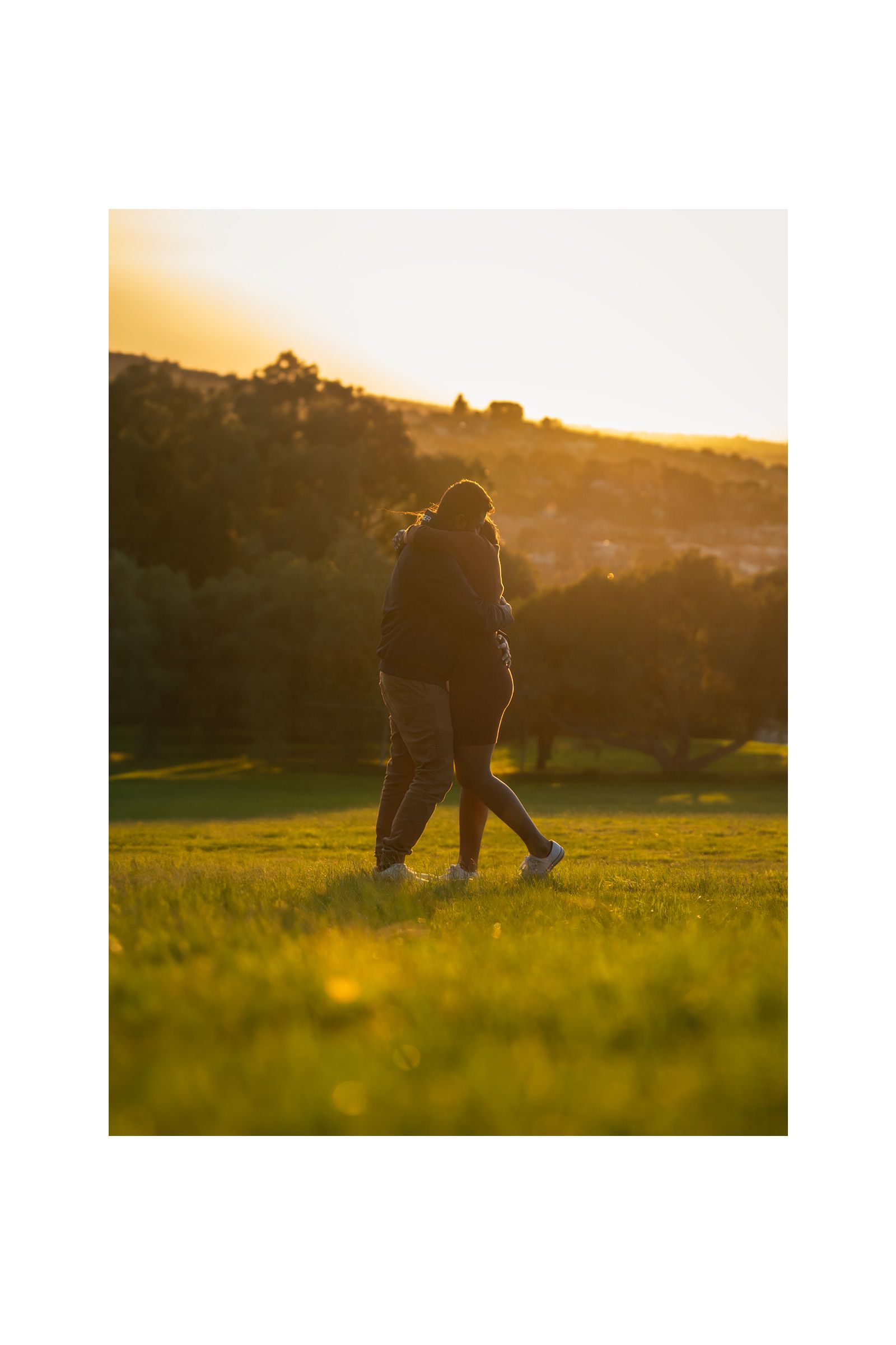 A couple is walking through a grassy field at sunset.