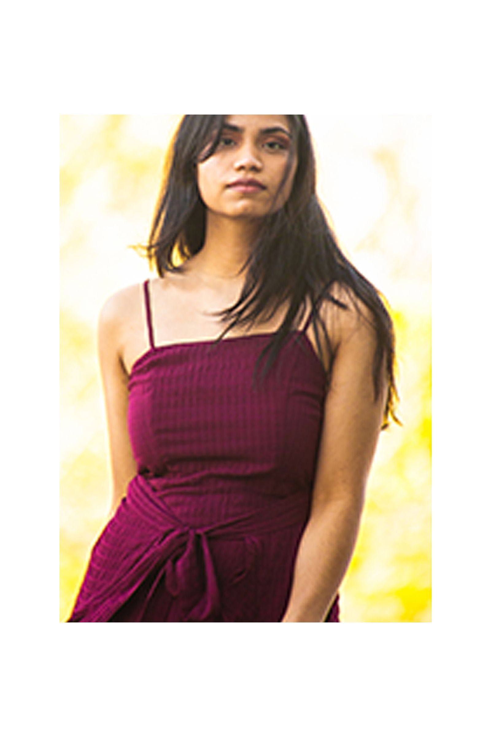 A woman in a purple dress is standing in front of a yellow background.