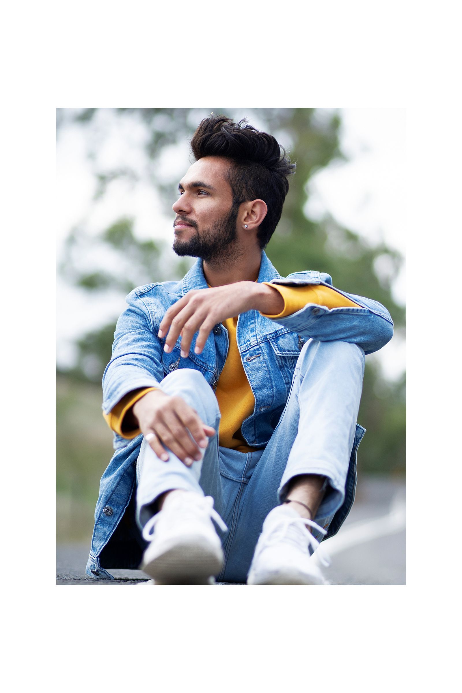 A man is sitting on the ground wearing a denim jacket and jeans.