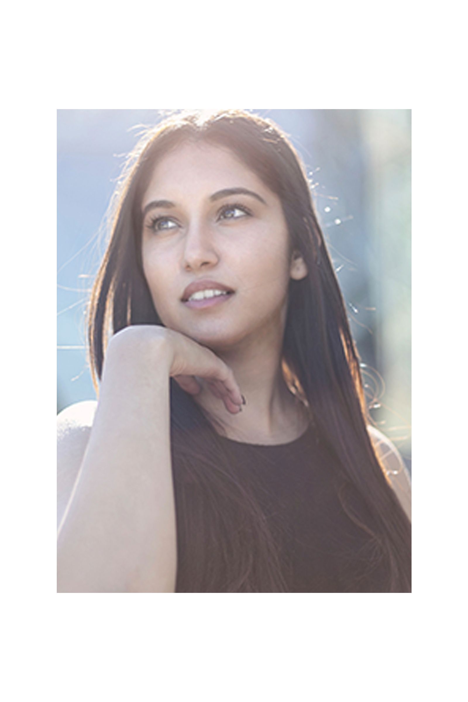 A woman with long hair is looking up with her hand on her chin.