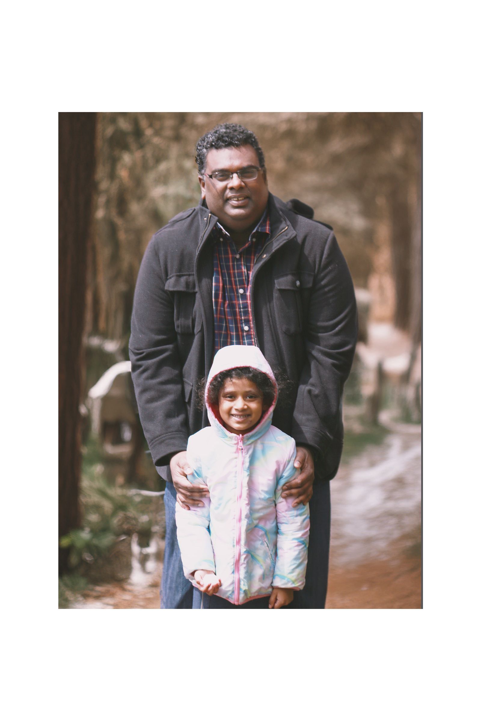 A man and a little girl are posing for a picture in the woods.