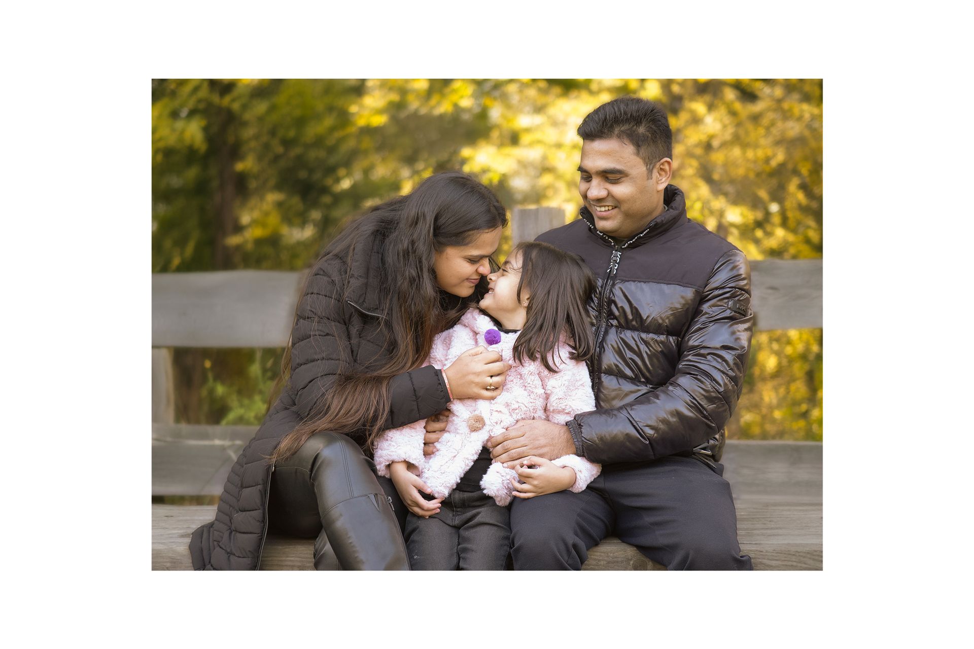 A man and woman are sitting on a bench with a little girl.