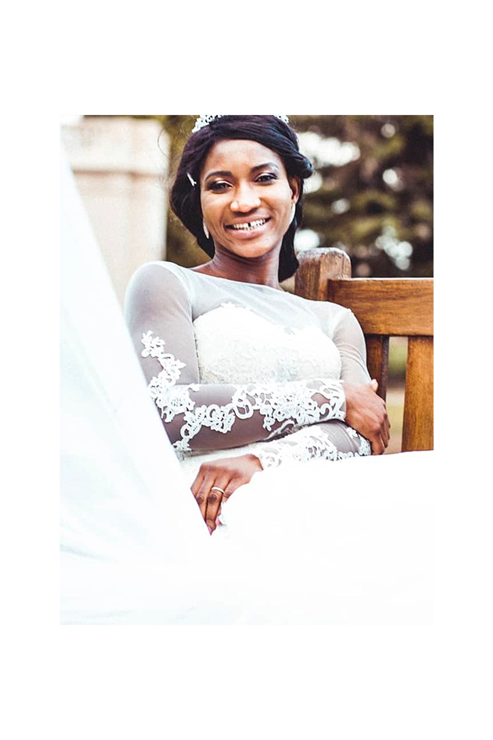 A woman in a wedding dress is sitting on a bench and smiling.