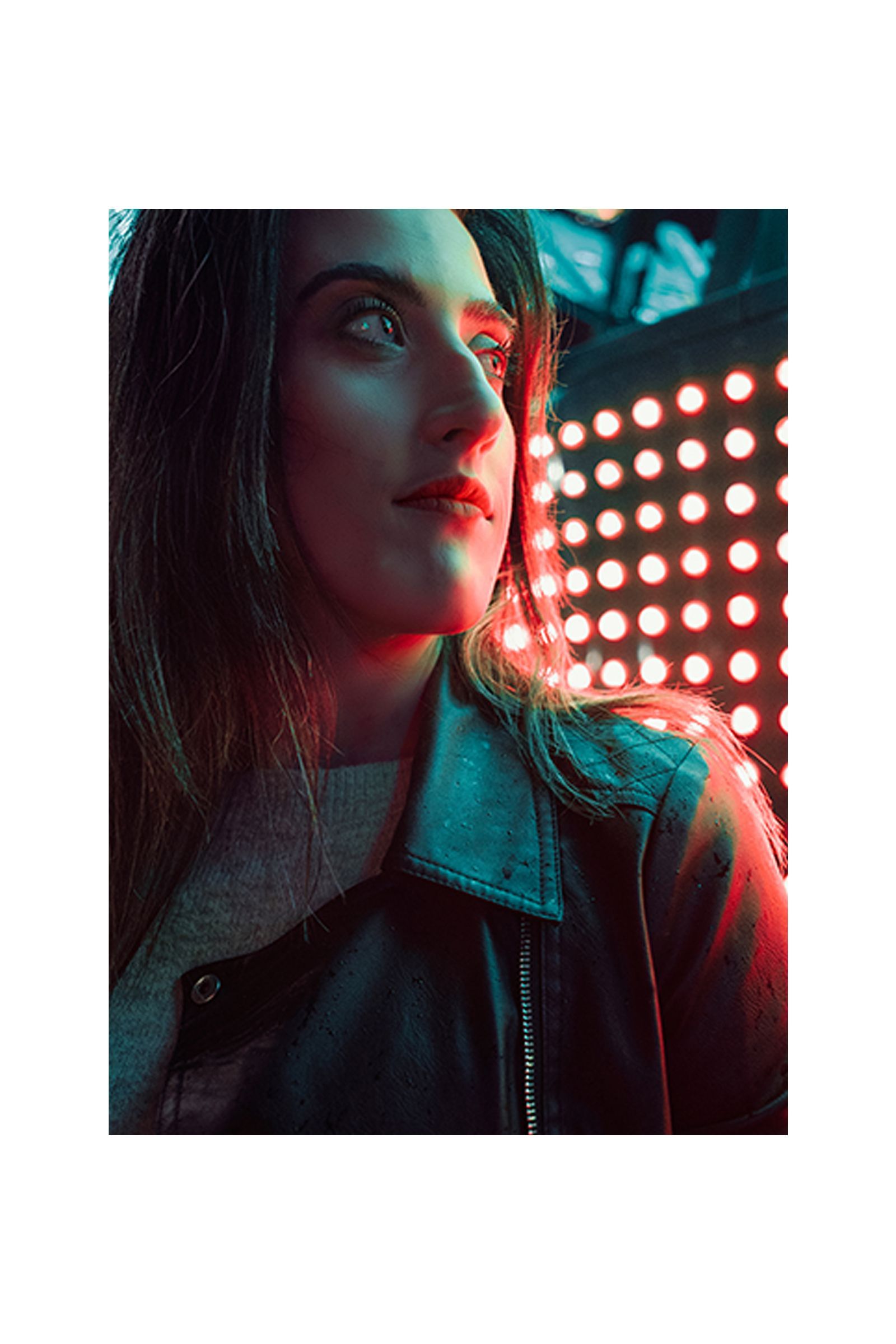 A woman in a leather jacket is standing in front of a wall of lights.