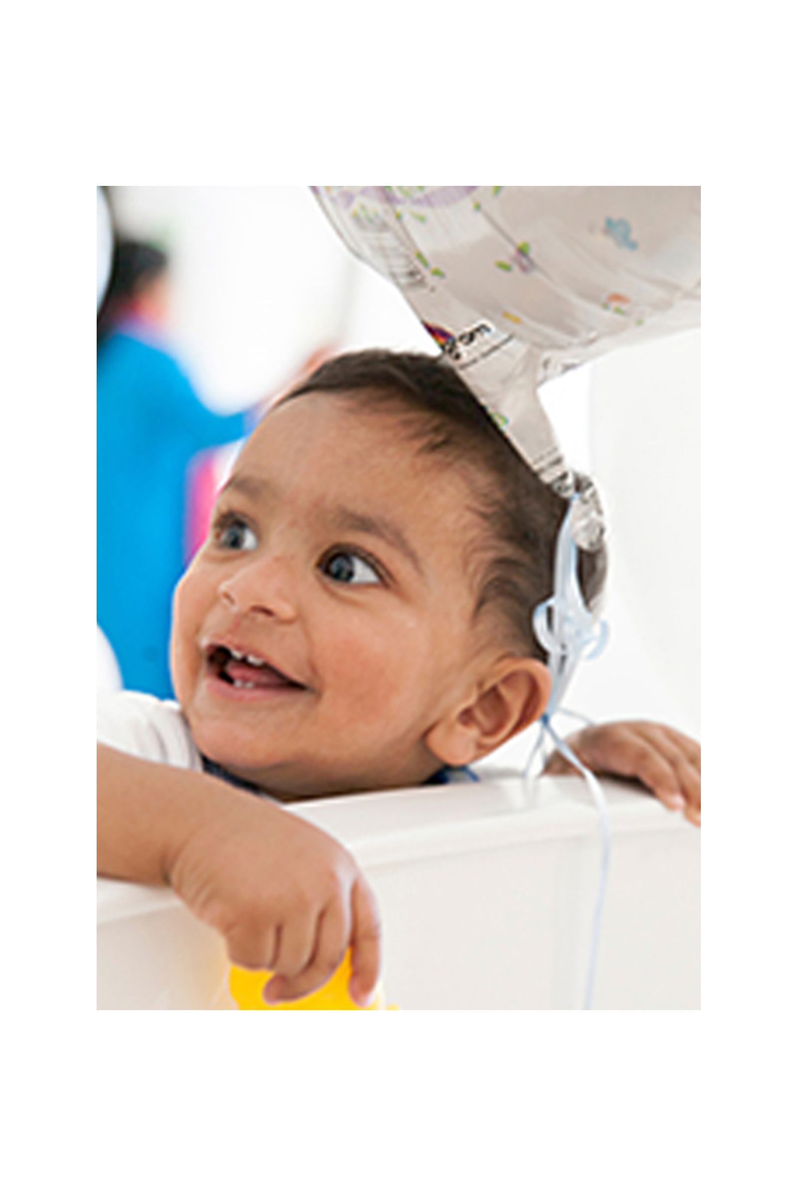 A baby is wearing a hat and smiling while sitting in a high chair.