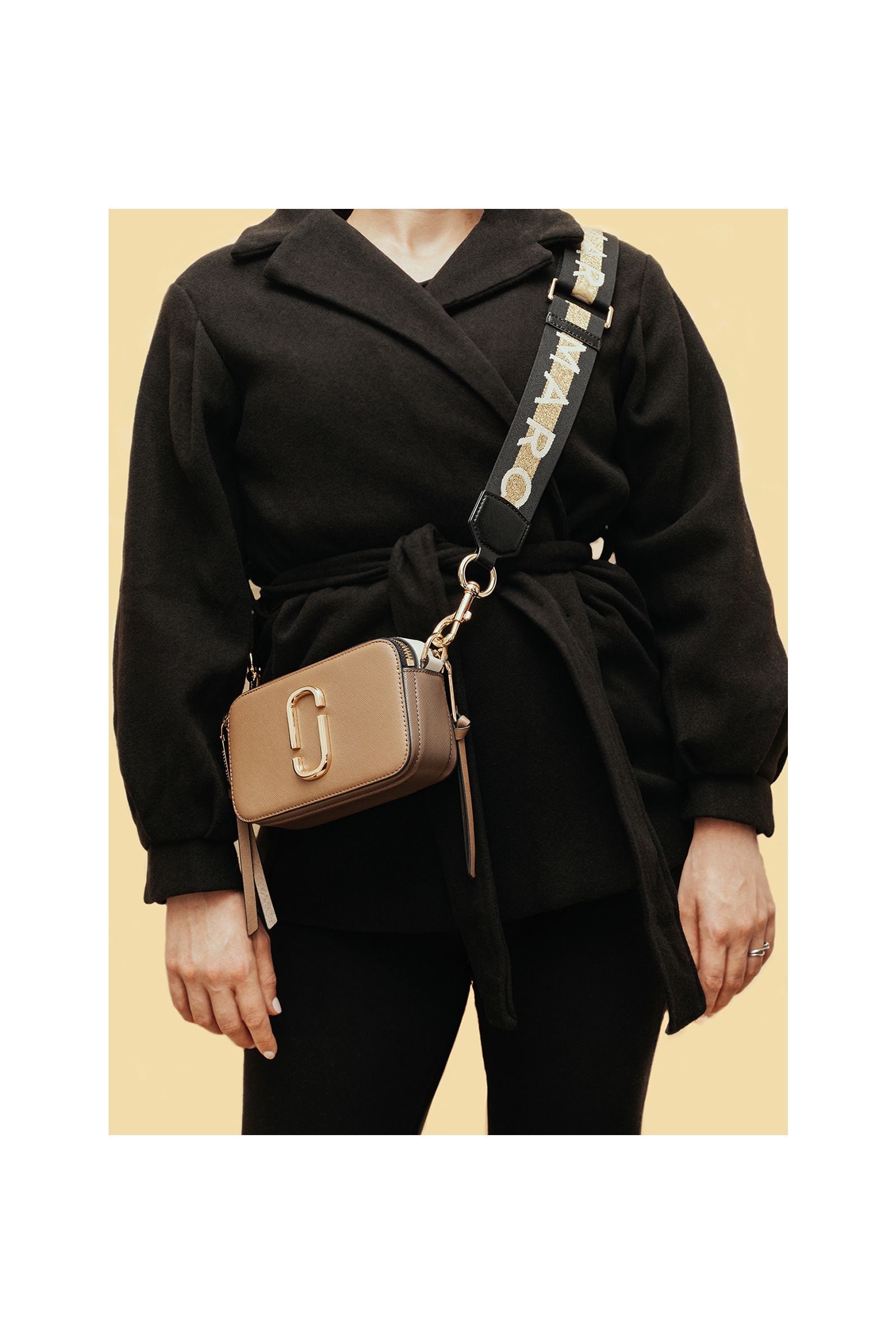 A woman wearing a black jacket and a brown purse with a s on it.