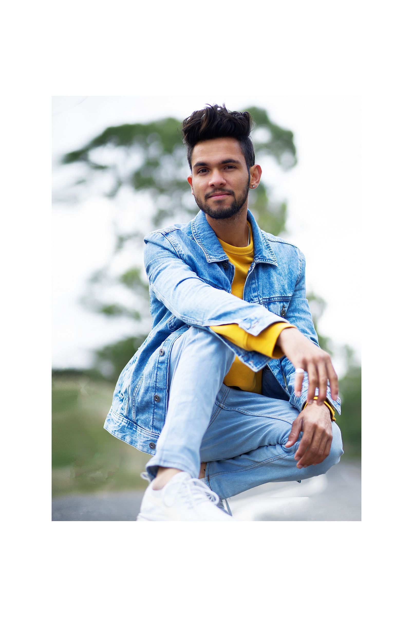 A man in a denim jacket and jeans is squatting down.