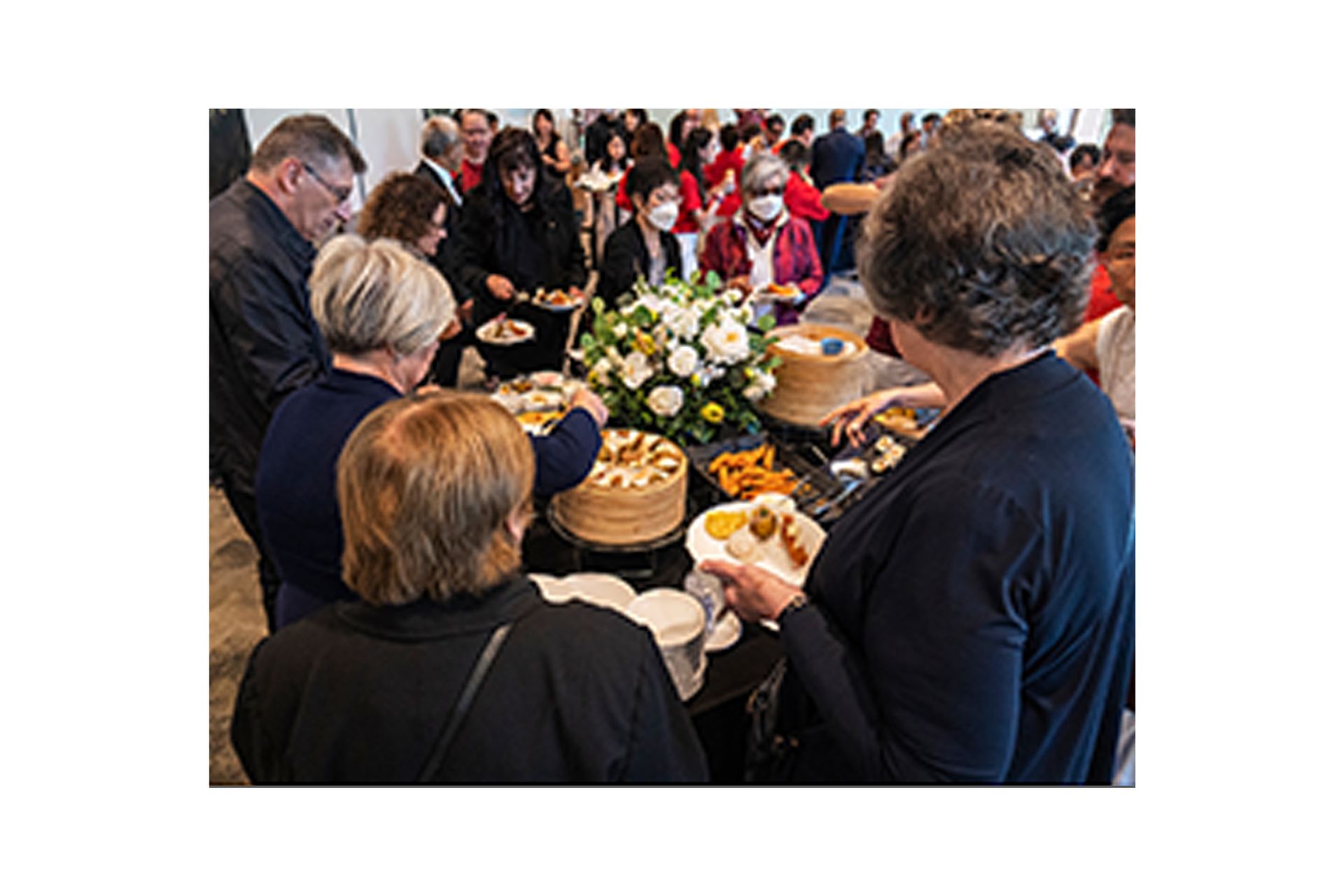 A group of people are standing around a table eating food.