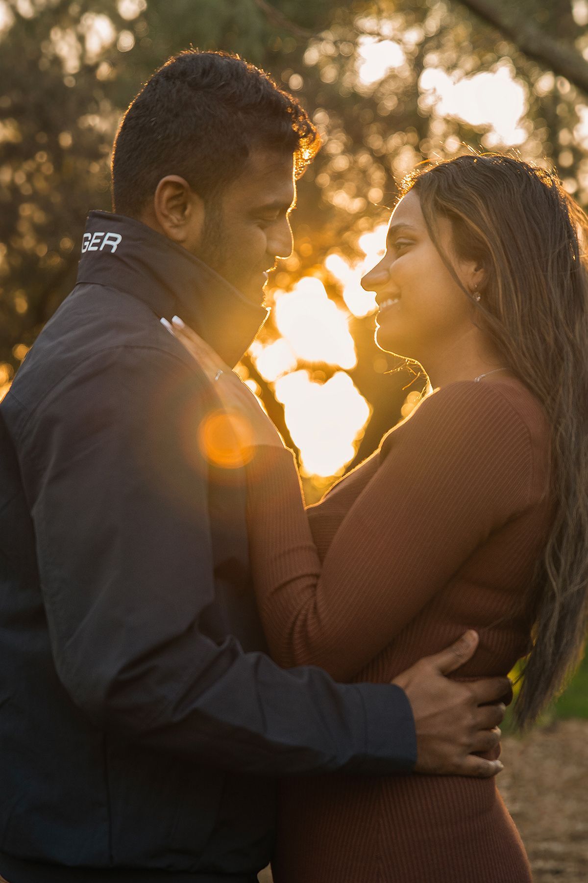 A man and a woman are hugging each other in front of a sunset.