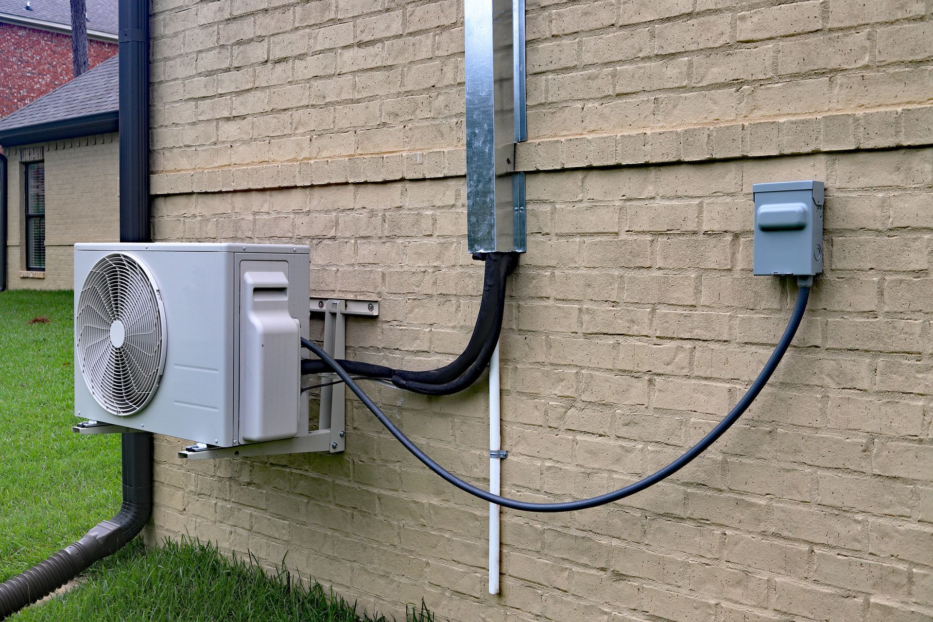 Outdoor HVAC unit and electrical boxes mounted on a tan brick wall with conduit and cables.