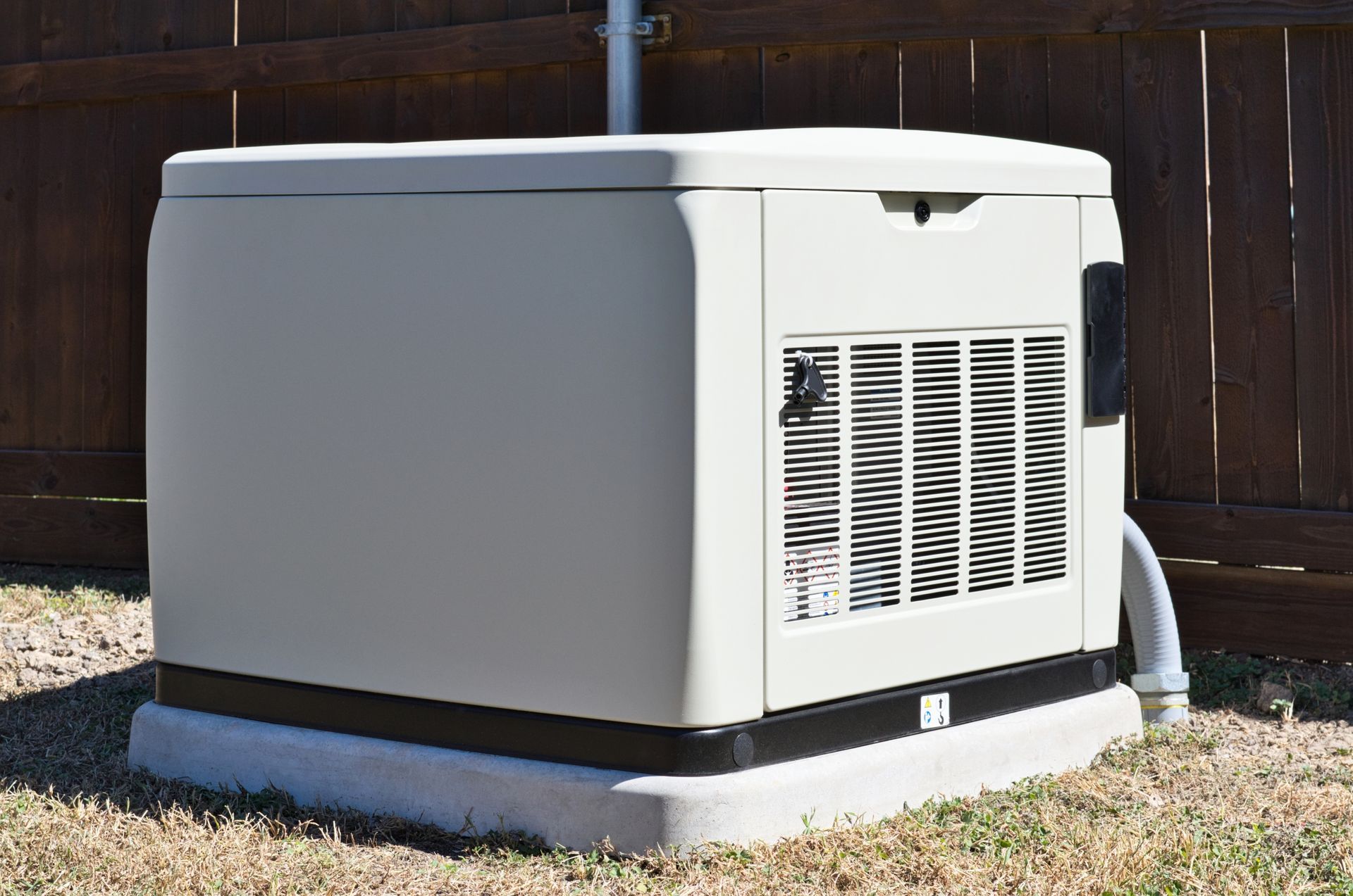 Outdoor home generator unit with gray housing and vented side panel beside a wooden fence