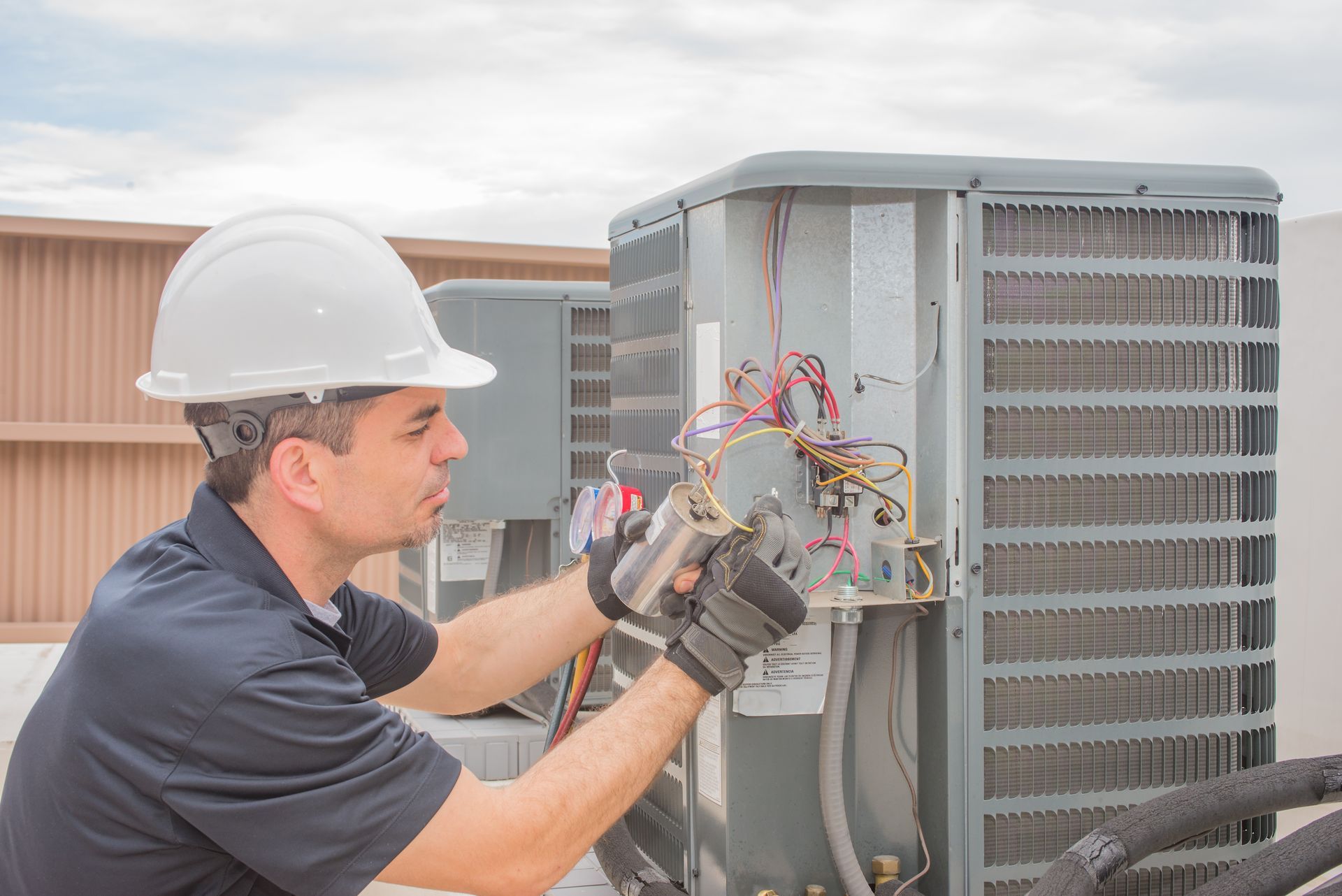 Technician in hard hat inspecting wiring on an outdoor HVAC unit