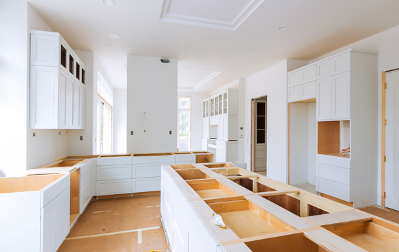 A kitchen under construction with white cabinets and wooden counter tops.