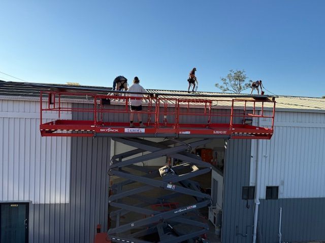 Four people working on a roof from a red scissor lift platform against a blue sky.