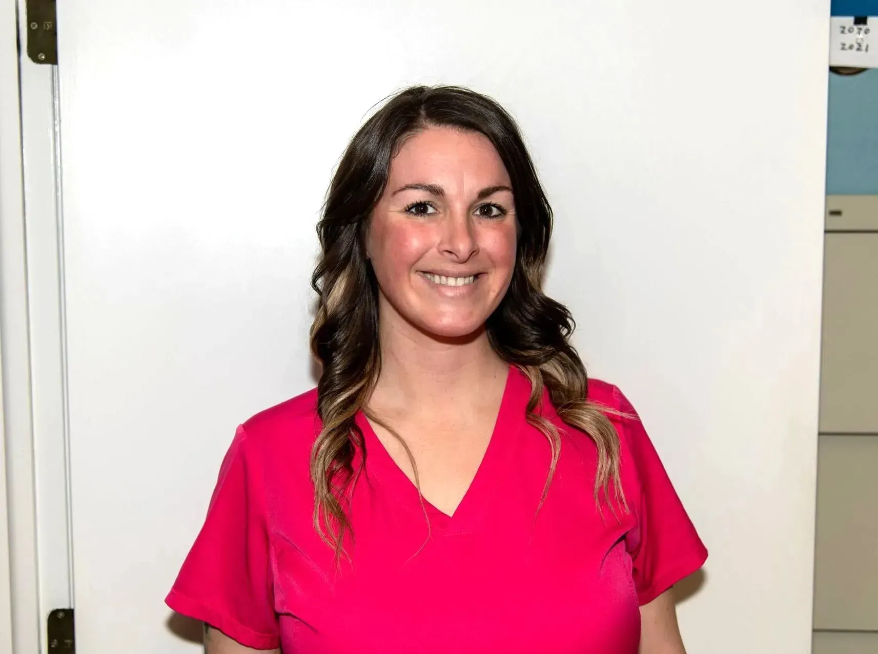 Smiling person in a bright pink shirt standing indoors against a white wall