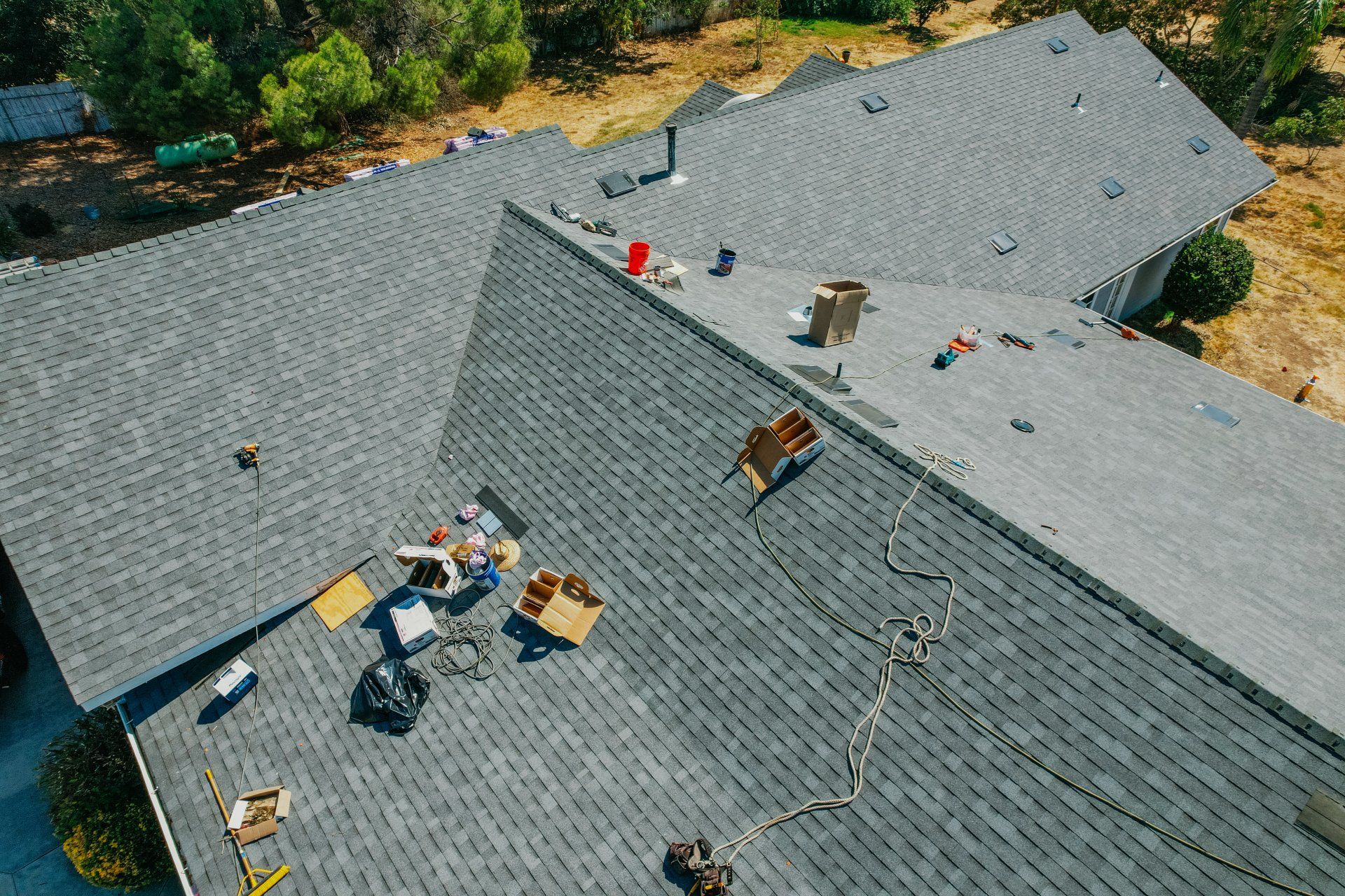 Overhead view of a gray shingle roof with construction debris scattered on the surface, under a blue sky.