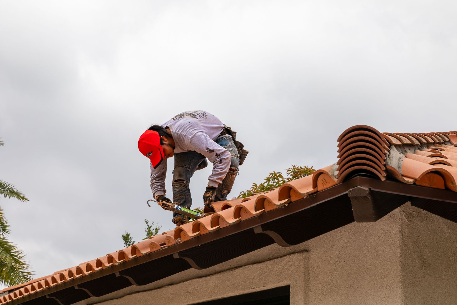 A man wearing a red hat is working on a tiled roof