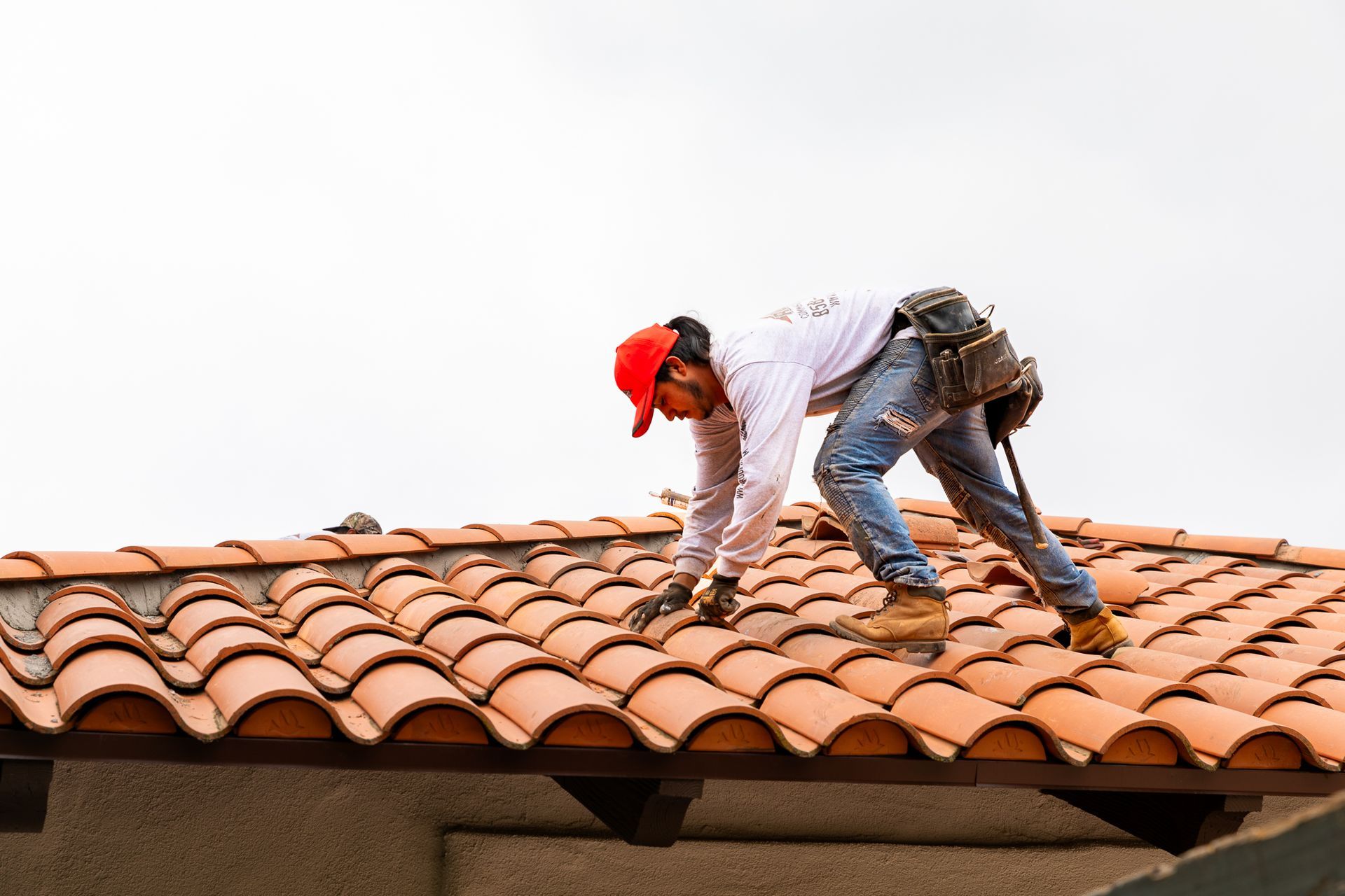 A man in a red hat is working on a tiled roof