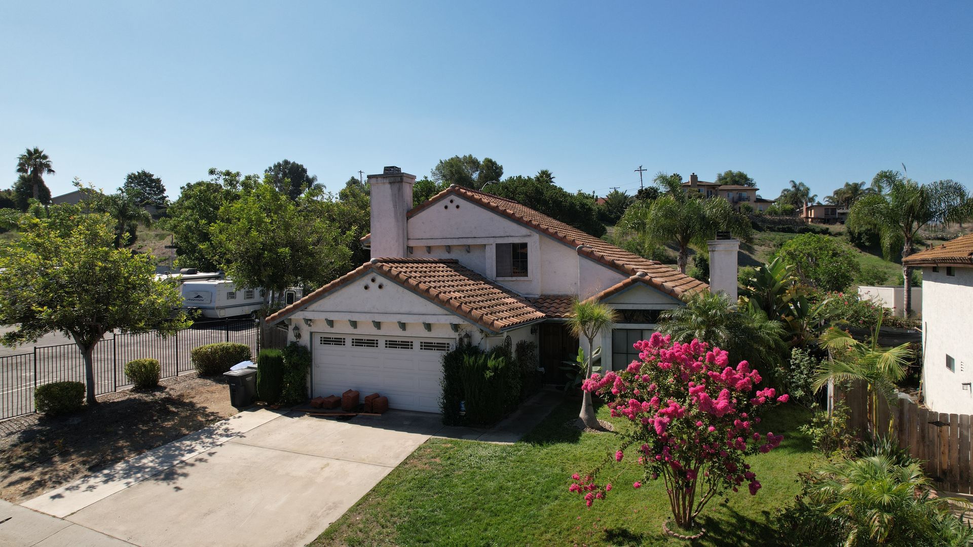 A white house with a red tile roof is surrounded by trees and bushes