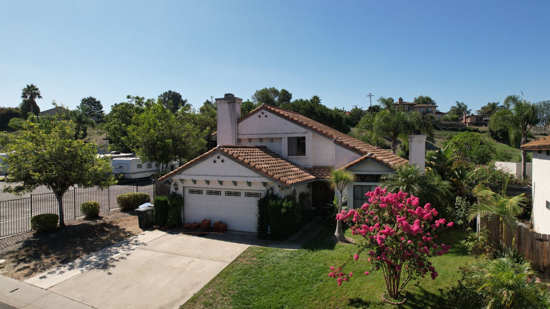 A white house with a red tile roof is surrounded by trees and bushes