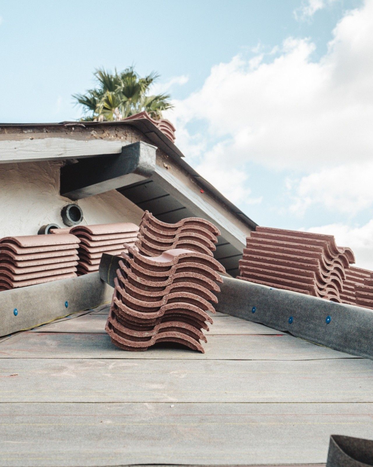 Stacked roof tiles on a sloped rooftop under a partly cloudy sky