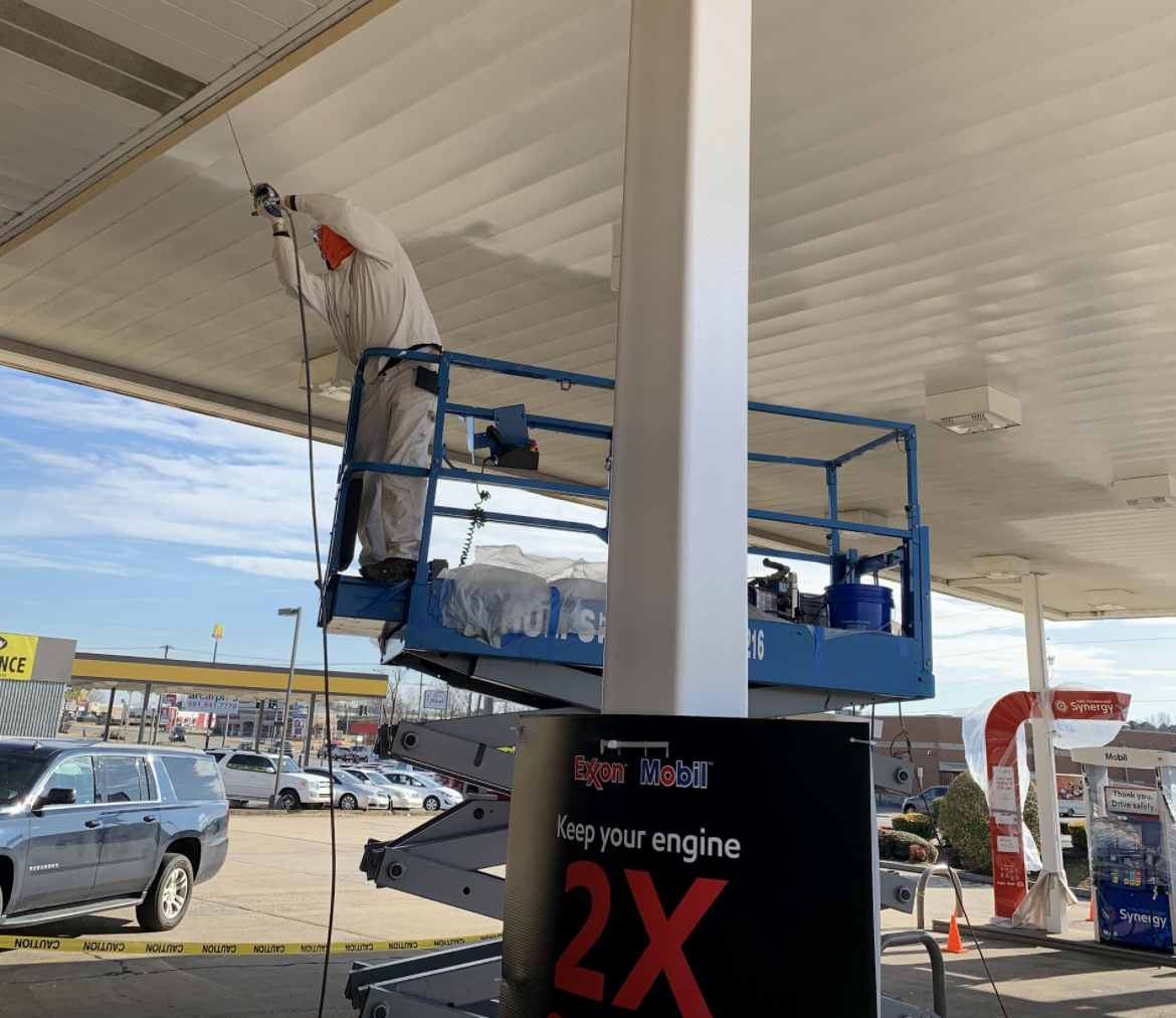 Mural of a colorful portrait on a tall building; a white building is beside it. The sky is blue.